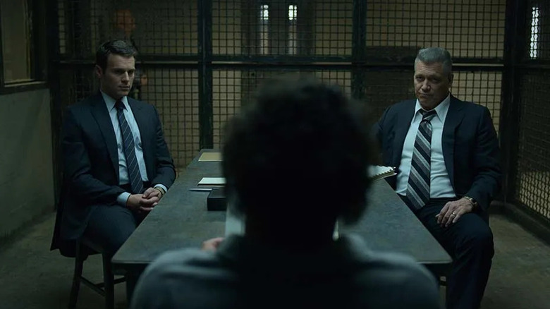 Holden Ford (Jonathan Groff) and Bill Tench (Holt McCallany) speak with a murderer at a table in a caged interrogation room on Mindhunter