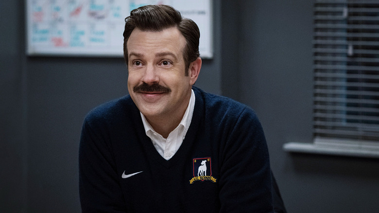 Ted Lasso (Jason Sudeikis) smiles in his office on Ted Lasso