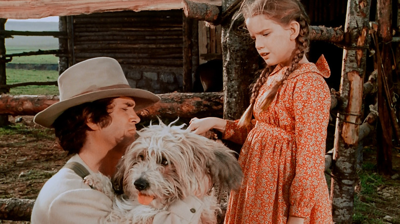 Charles Ingalls (Michael Landon) holds a dog by a fence with Laura Ingalls (Melissa Gilbert) in Little House on the Prairie