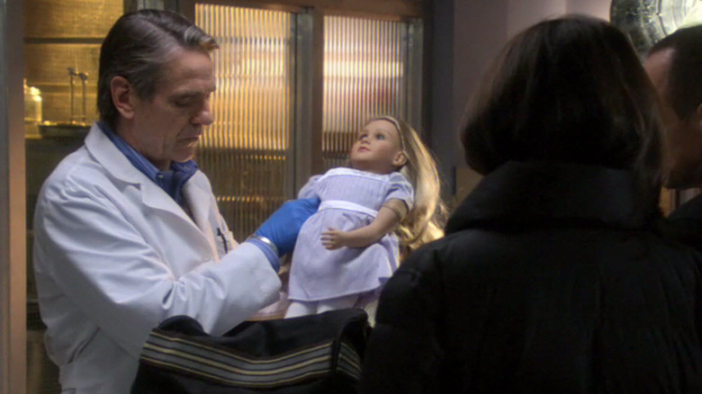 Cap (Jeremy Irons) holding a doll and showing Olivia (Mariska Hargitay) on Law & Order: Special Victims Unit