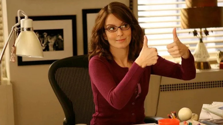 Liz Lemon (Tina Fey) gives two thumbs up from her desk in 30 Rock