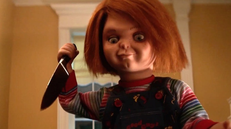 Chucky (Brad Dourif) holds a kitchen knife while smiling in Chucky
