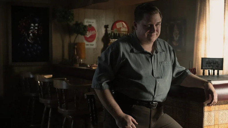 John Wayne Gacy (Michael Chernus) smiles knowingly at a darkened bar in Devil in Disguise: John Wayne Gacy