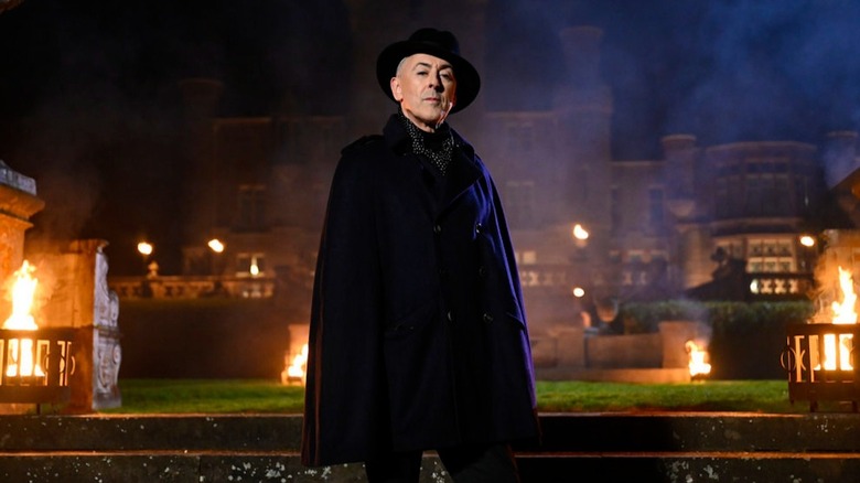 Alan Cumming stands in front of an ominously lit castle in The Traitors