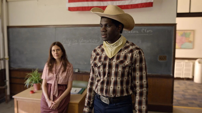 Iwegbuna (Conphidance) stands in a classroom wearing a cowboy outfit on Little America