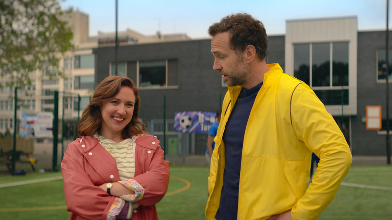 Jason Ross (Rafe Spall) speaks with a smiling Nikki Newman (Esther Smith) on a school athletic field on Trying