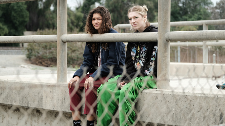 Rue (Zendaya) and Jules (Hunter Schafer) sitting outside behind a fence not talking on Euphoria