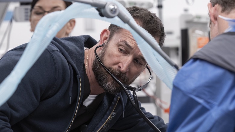 Dr. Robby (Noah Wyle) wearing his stethoscope listening with tubes in front of him on The Pitt