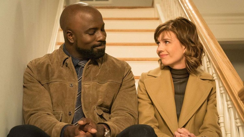 Mike Colter and Katja Herbers as  David Acosta and Dr. Kristen Bouchard, sitting together on the steps and smiling in Evil