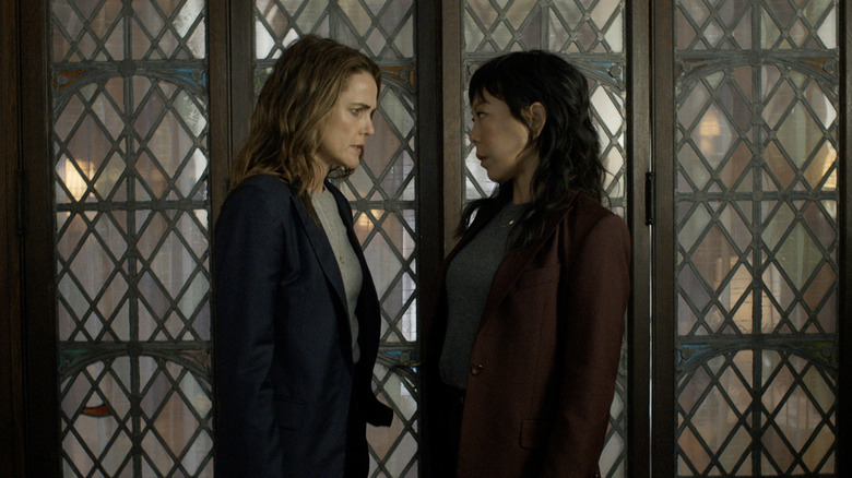 Eidra Park and Kate Wyler meet beside a large window in "The Diplomat" (2023)