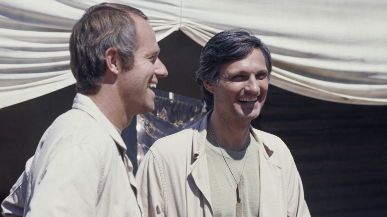 Mike Farrell as B.J. Hunnicutt and Alan Alda as Benjamin Franklin "Hawkeye" Pierce laughing while filming an episode of MASH