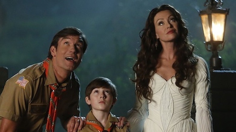 Jerry O'Connell as Herman and Mason Cook as Eddie, both in Boy Scout uniforms, standing next to Portia de Rossi as Lily in a white dress next to a street lamp as they all look up at something in Mockingbird Lane