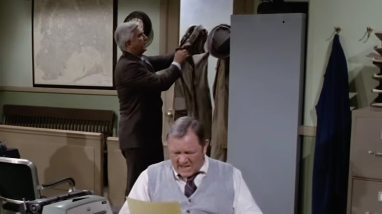 Frank Drebin hanging coat and hat in Police Squad headquarters while Ed scowls at typewriter