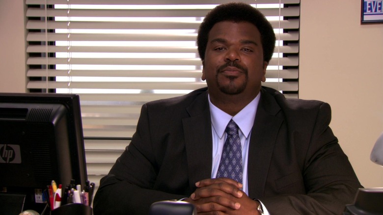 Craig Robinson as Darryl Philbin, sitting at his desk in a suit on The Office.