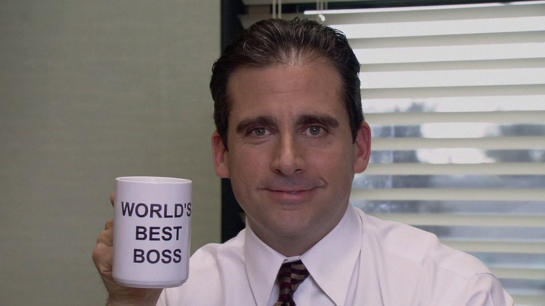 Steve Carell as Michael Scott, holding up his World's Best Boss coffee mug with a smile on The Office.