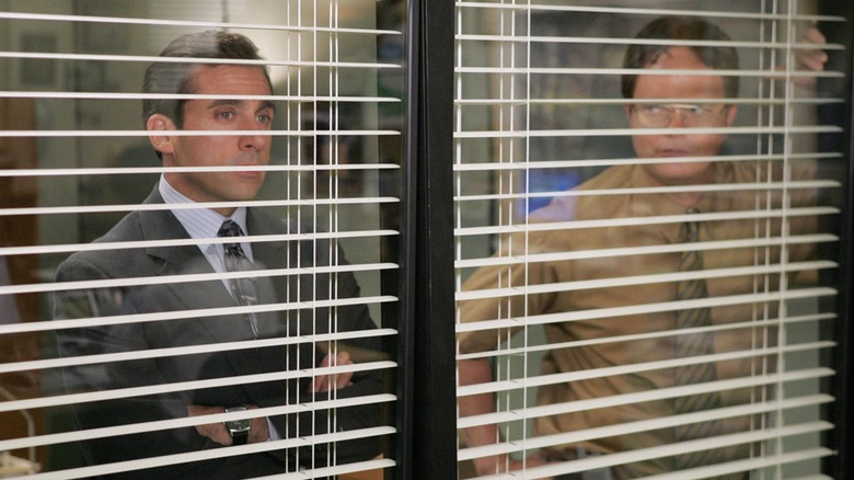 Steve Carell and Rainn Wilson as Michael Scott and Dwight Schrute, staring through the blinds of Michael's office on The Office.