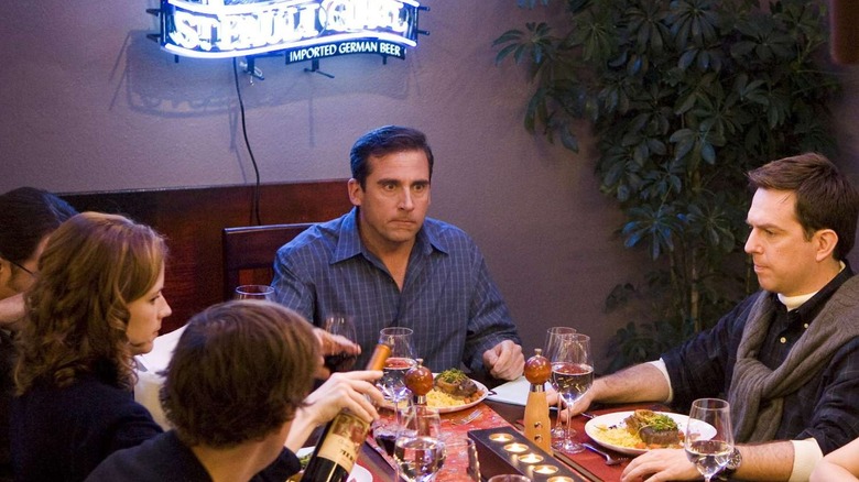 Steve Carell as Michael Scott, sitting at the head of his full dinner table, backlit by a neon beer sign on The Office.