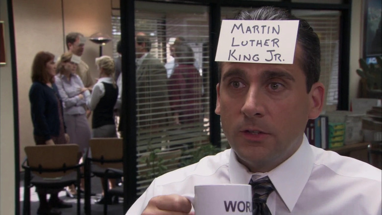 Michael Scott (Steve Carell) holds a coffee mug while wearing a notecard on his forehead labeling himself Martin Luther King, Jr. in The Office