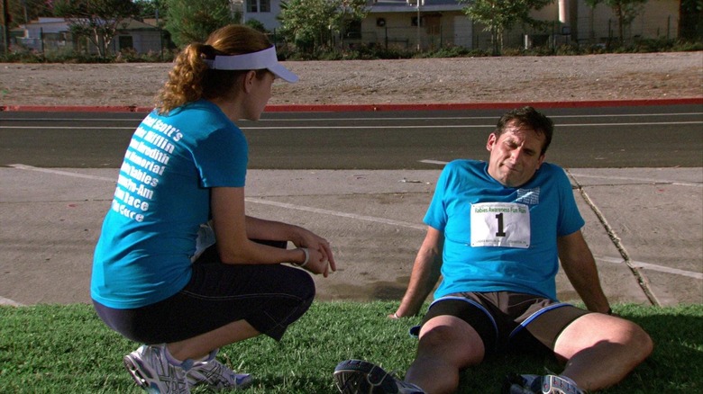 Pam Beesly (Jenna Fischer) crouches near a sickened Michael Scott (Steve Carell) sitting on grass in The Office