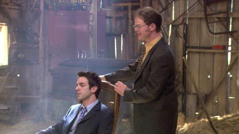 Ryan Howard (BJ Novak) sits in a rocking chair held by Dwight Schrute (Rainn Wilson) in The Office