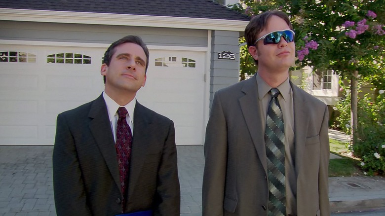 Michael Scott (Steve Carell) and Dwight Schrute (Rainn Wilson) in stylish sunglasses stand in front of Michael's garage in The Office
