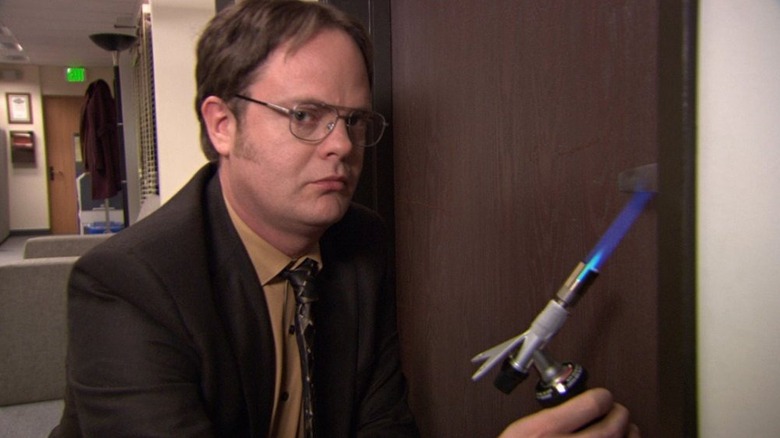 Dwight Schrute (Rainn Wilson) glances at the camera while blowtorching a door handle in The Office