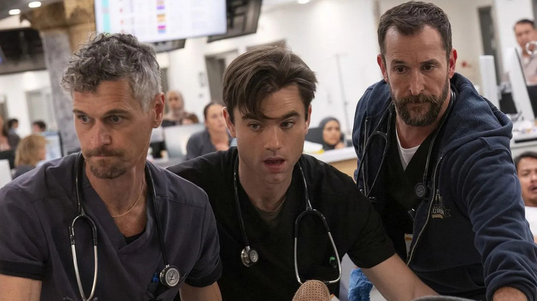 Ned Brower as nurse Jesse Von Horn, Patrick Ball as Dr. Frank Langdon, and Noah Wyle as Dr. Robby Robinavitch moving a patient around the ER as people watch on in The Pitt