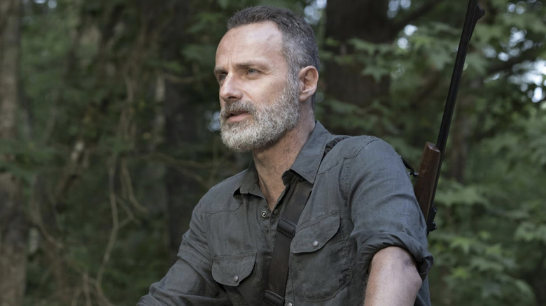 Rick Grimes with a grey beard looking into the distance with a rifle on his back