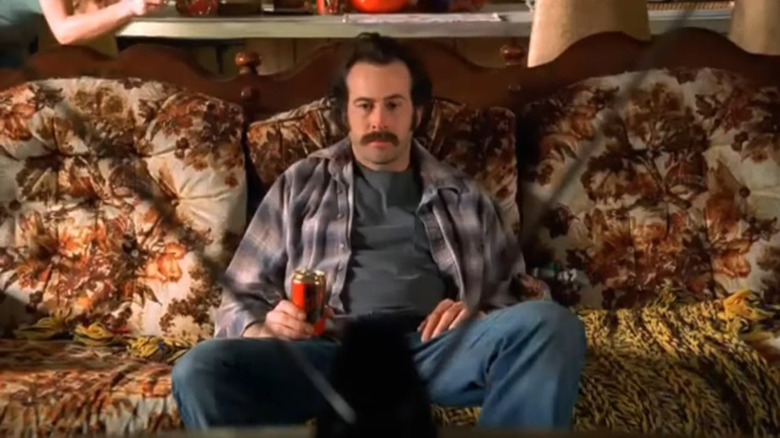 Earl Hickey (Jason Lee) sits on a vintage couch while holding a beer can and staring at the TV in "My Name Is Earl"