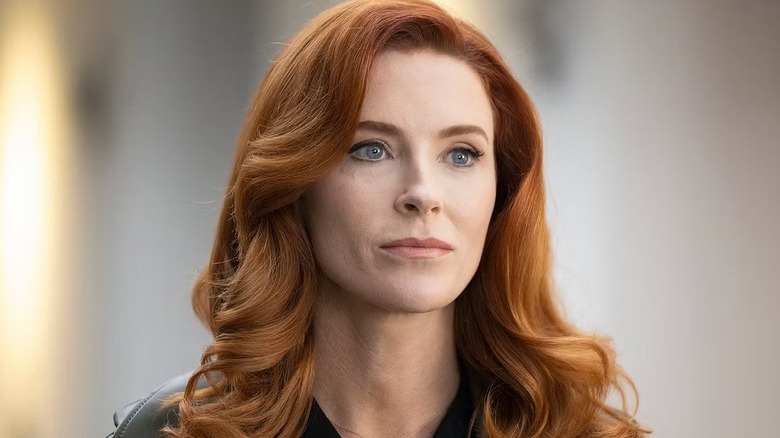 Monica (Bridget Regan) gri boyalı bir odada duruyor. 