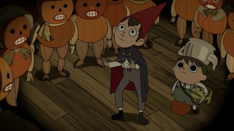 Wirt holds his hands up defensively as Greg stands beside him holding a frog under his arm while the two are surrounded by blank faced Pumpkin People in "Over the Garden Wall"