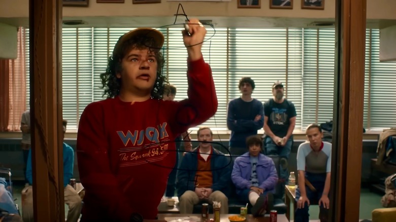 Dustin drawing on a glass pane in front of his friends who watch on
