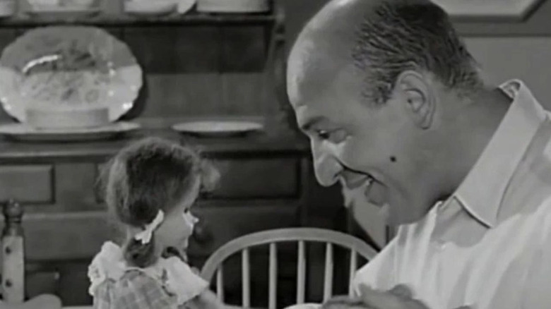 Erich Streator (Telly Savalas) smiles staring at a girl doll in The Twilight Zone