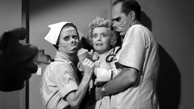 Two doctors with pig-like facial features hold a scared woman in "The Twilight Zone" episode "Eye of the Beholder" (1960). A hand holding a syringe can be seen in the foreground.