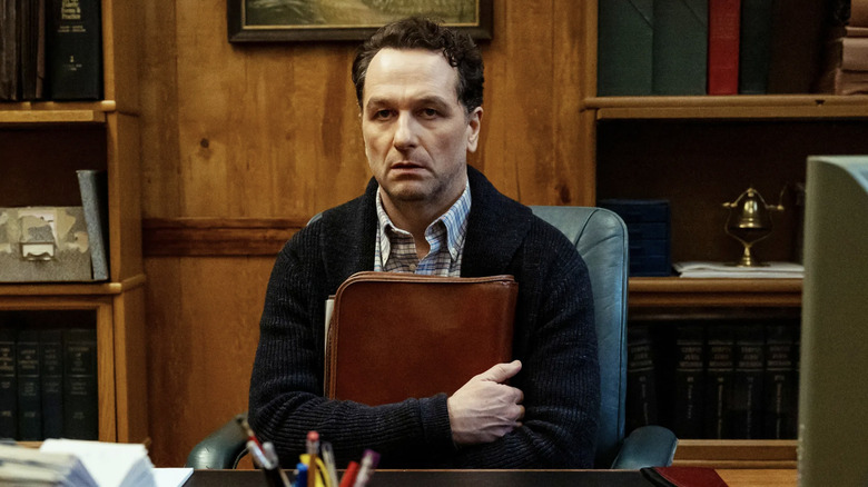 Mayor Loftis clutching a brown leather bag in his office in Widow's Bay (2026)
