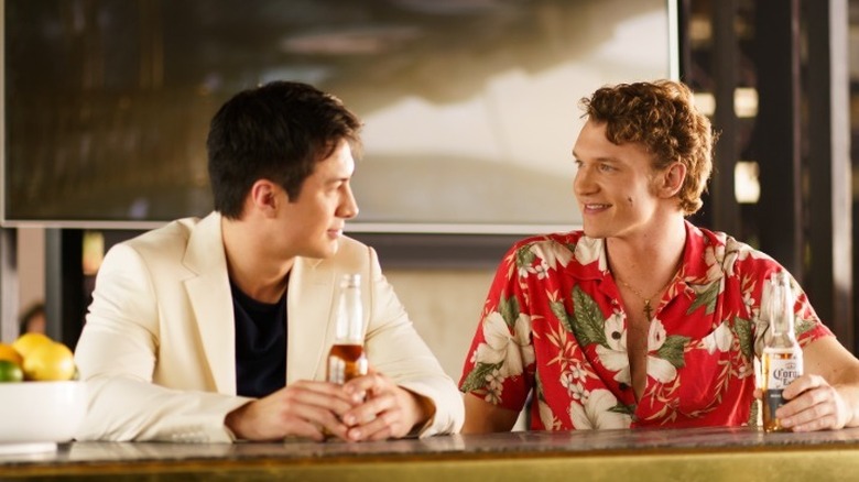 Shane and Ilya holding drinks sitting at a counter in 'Heated Rivalry'