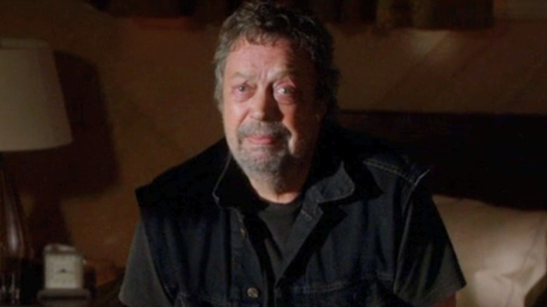 Billy Flynn looks at the screen in a denim, sleeveless jacket and t-shirt.