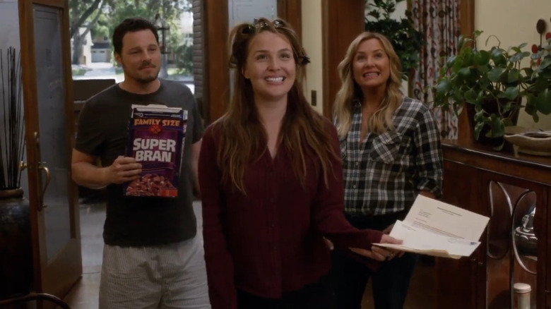 Camilla Luddington grinning with pieces of paper in hand in front of Justin Chambers as Alex Karev holding cereal box and Jessica Capshaw as Arizona Robbins grinning on Grey's Anatomy