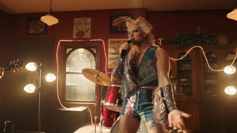 Casey Cott as Kevin dressed as Hedwig with blonde wig, shorts, and vests singing with microphone in front of drum set on Riverdale