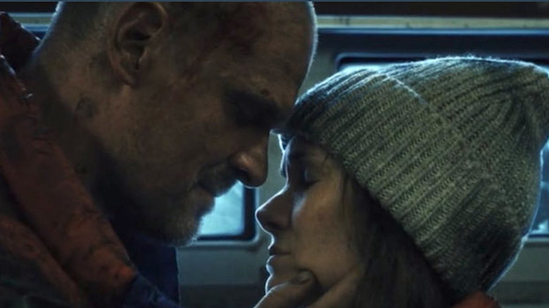 David Harbour as Hopper with shaved head with blood on it leaning in towards Winona Ryder as Joyce closing her eyes with beanie on Stranger Things