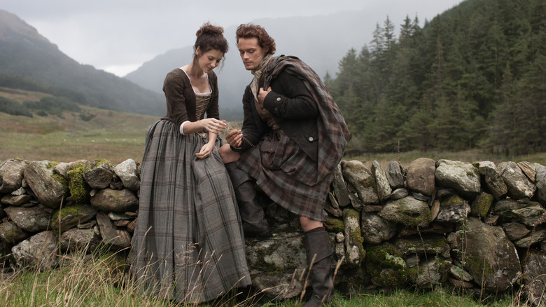 Claire and Jamie sitting on stone wall
