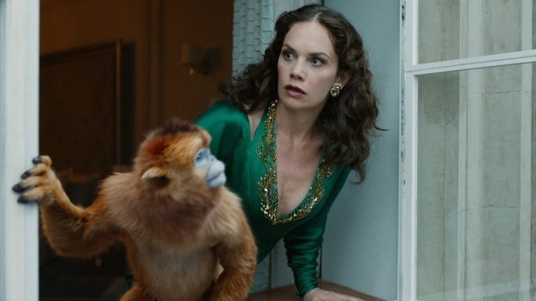 Ruth Wilson as Marisa Coulter looking out window alongside orange monkey in His Dark Materials