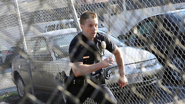 Ben Sherman (Ben McKenzie) runs frantically behind a chained link fence in Southland