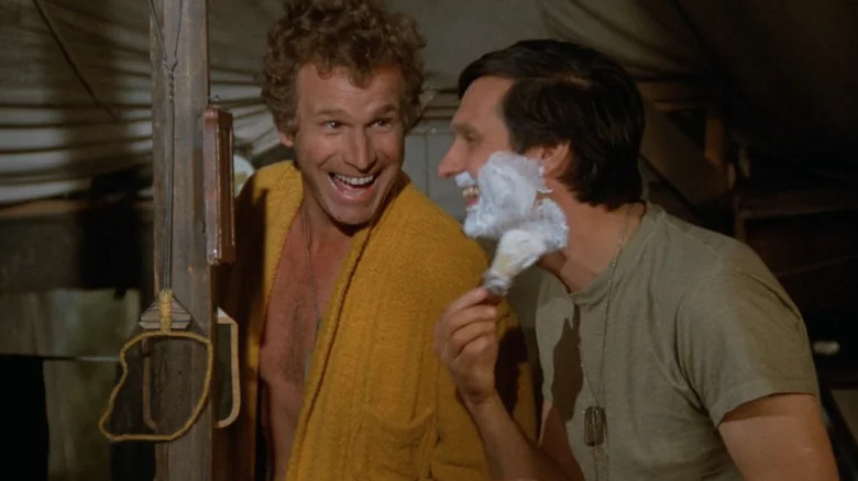 Trapper John McIntyre (Wayne Rogers) smiles at Hawkeye Pierce (Alan Alda) as he lathers up to shave in M*A*S*H