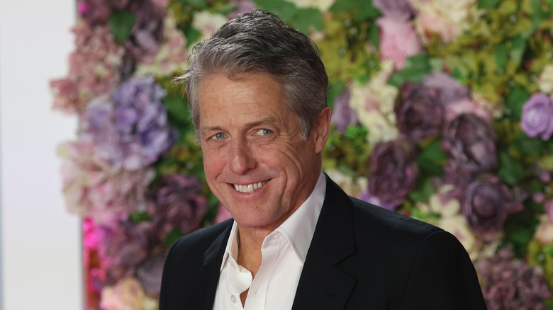 Hugh Grant posing in front of a floral arrangement