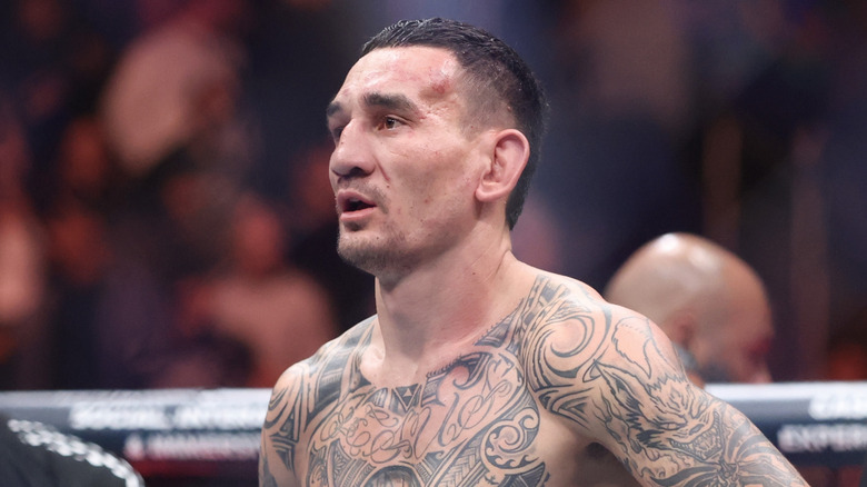 Max Holloway standing in a ring, large tribal tattoos across his chest and shoulders.
