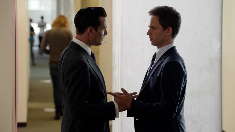 Mike Ross and Harvey Specter conversing in a hallway and pointing at one another