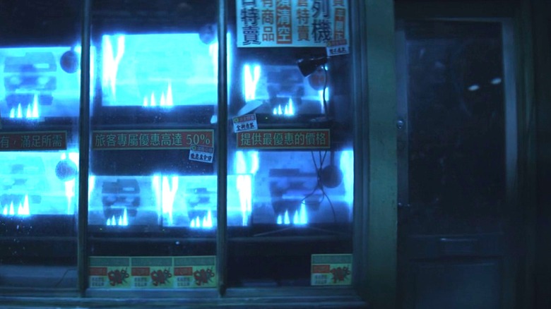 Two rows of TVs with blue flickering lights next to a window where a bright-eyed person is looking in in "VisionQuest" episode six.