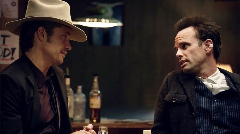 Raylan Givens wears a white cowboy hat whiel staring down Boyd Crowder, leaning against the bar in a tweed jacket, in "Justified"