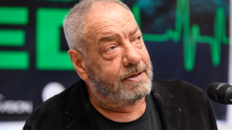 Close-up of Dick Wolf speaking to a mic and in front of a blurred green and black background